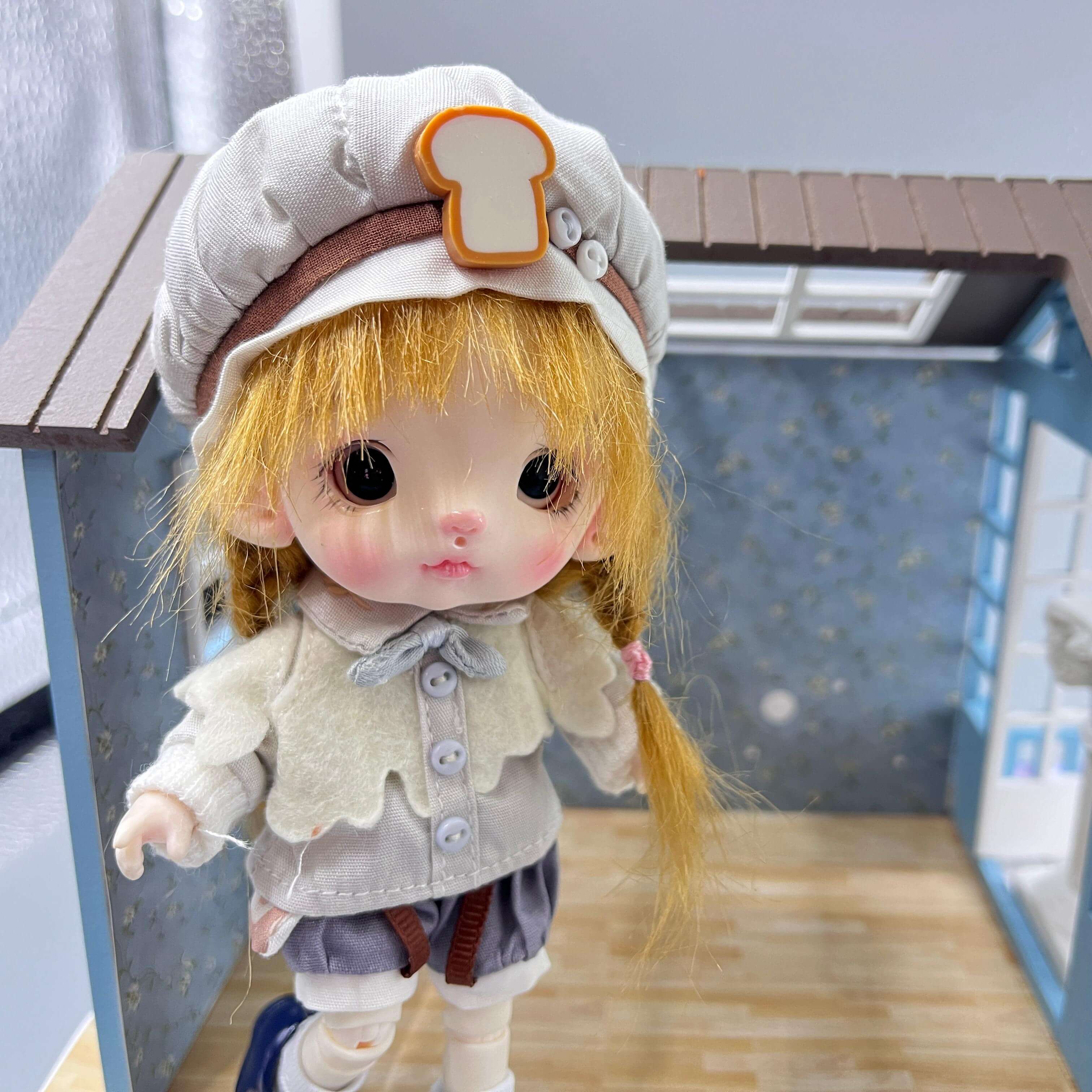 ball jointed doll with a hat resembling bread in a miniature room setting